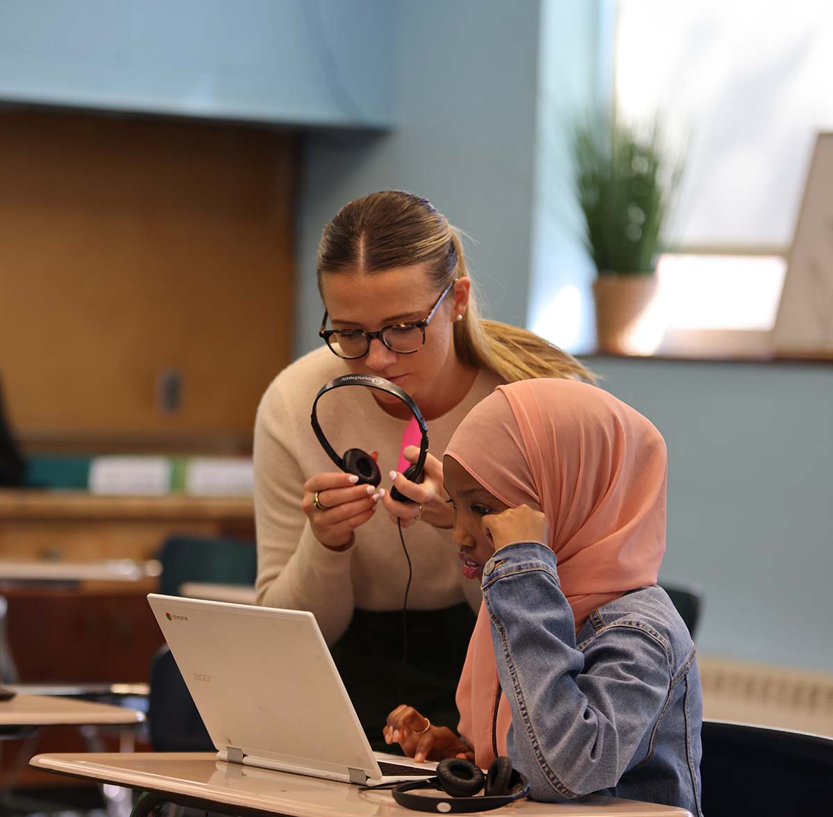 HSA Teacher smiles while kneeling beside a young student in a classroom setting.